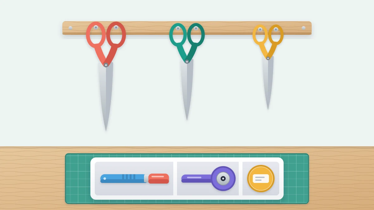 Three pairs of scissors hanging closed on wall hooks above a tray holding a capped craft knife, a rotary cutter with its guard closed and a small lidded container